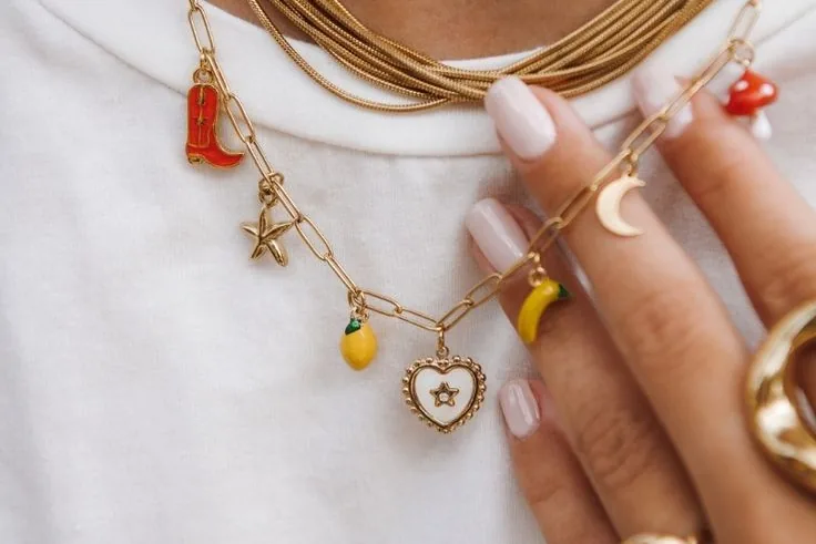 Un collier doré à charms porté sur un tee-shirt blanc : une botte, une étoile, un citron, un cœur, une lune et une banane