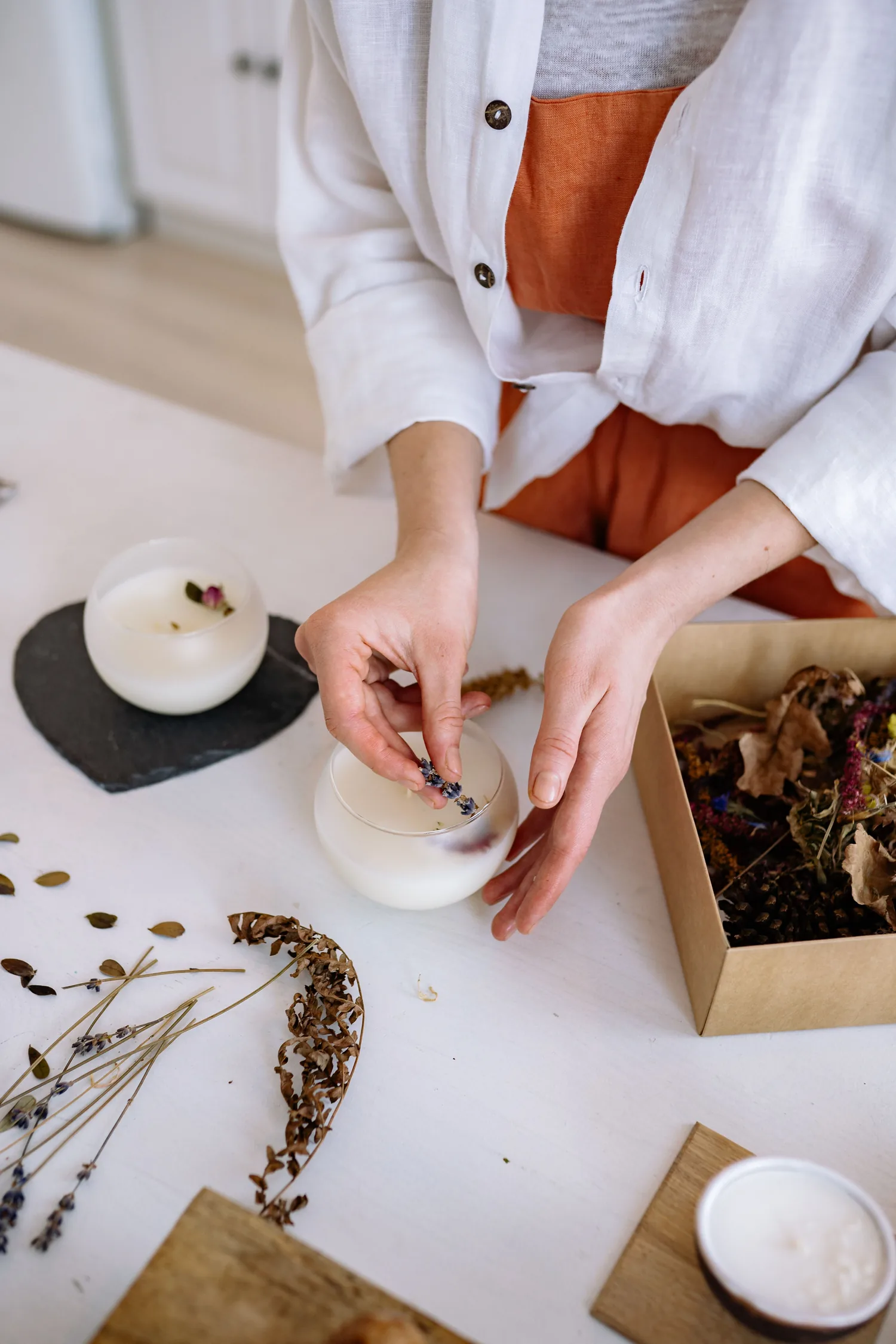 Deux mains posent un brin de lavande sur une bougie coulée dans un verre, fleurs séchées autour, EVJF à Bordeaux