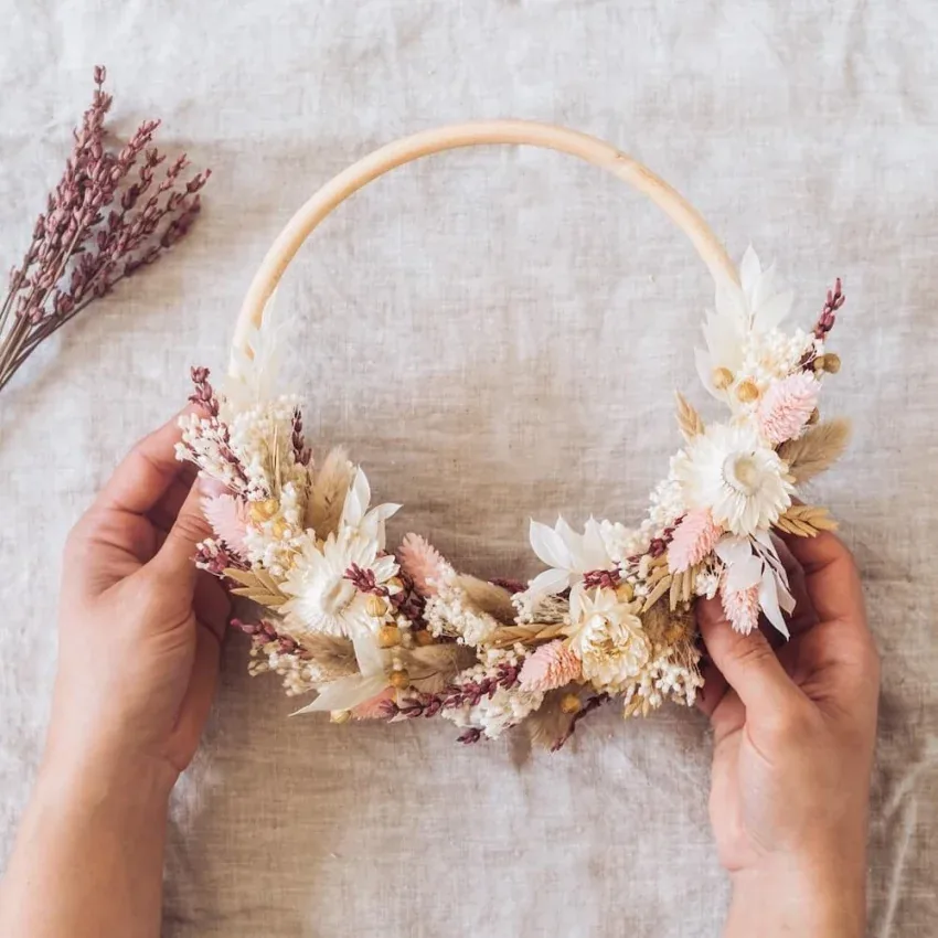 Deux mains présentent une couronne de fleurs séchées, dans des roses et des crèmes, sur une toile de lin, EVJF à Bordeaux