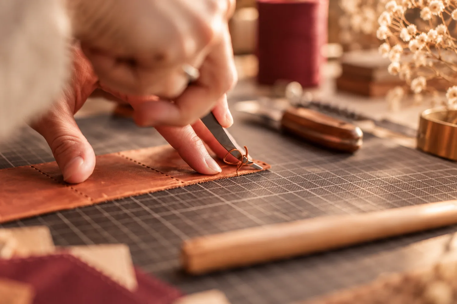 Une main découpe au tranchet une bande de cuir couleur cognac sur un tapis de coupe quadrillé
