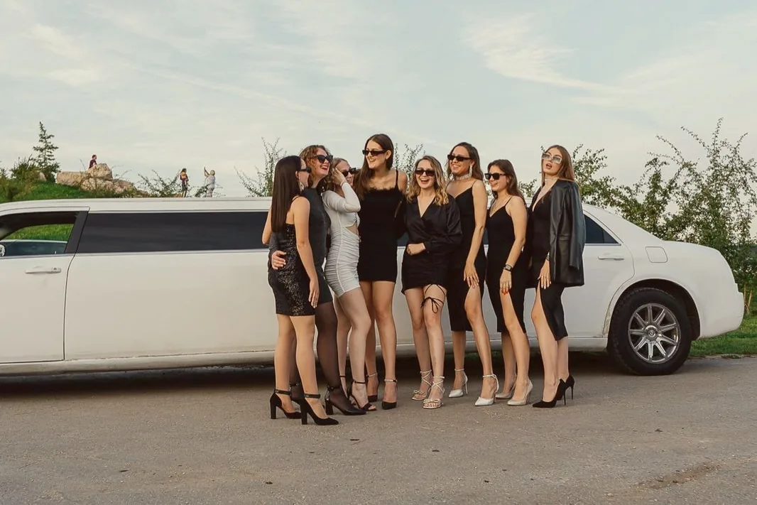Le groupe de copines en robes noires et lunettes de soleil pose devant une limousine blanche
