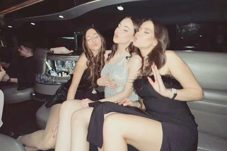 Trois copines en robe de soirée, yeux fermés, envoient un bisou sur la banquette de cuir
