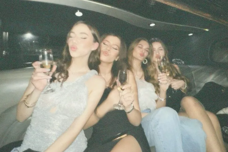 Quatre copines serrées sur la banquette de la limousine, coupe de champagne à la main, font un bisou à l'objectif