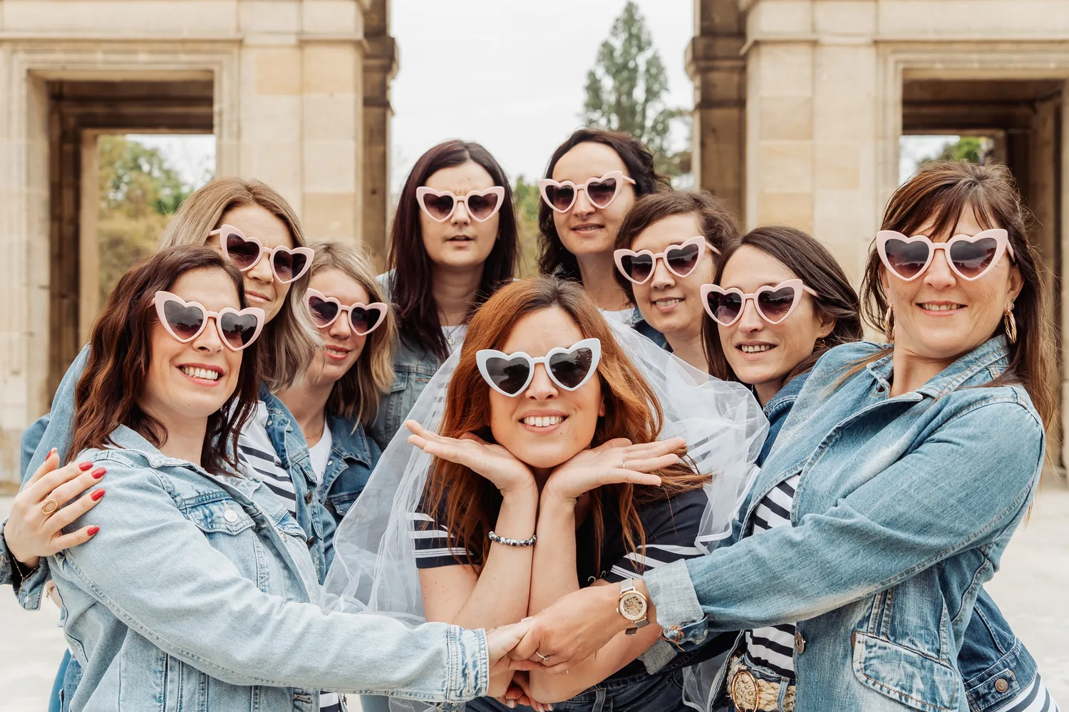 Le groupe serré en vestes en jean et lunettes en forme de cœur, la mariée au centre, mains croisées sous le menton, EVJF à Bordeaux