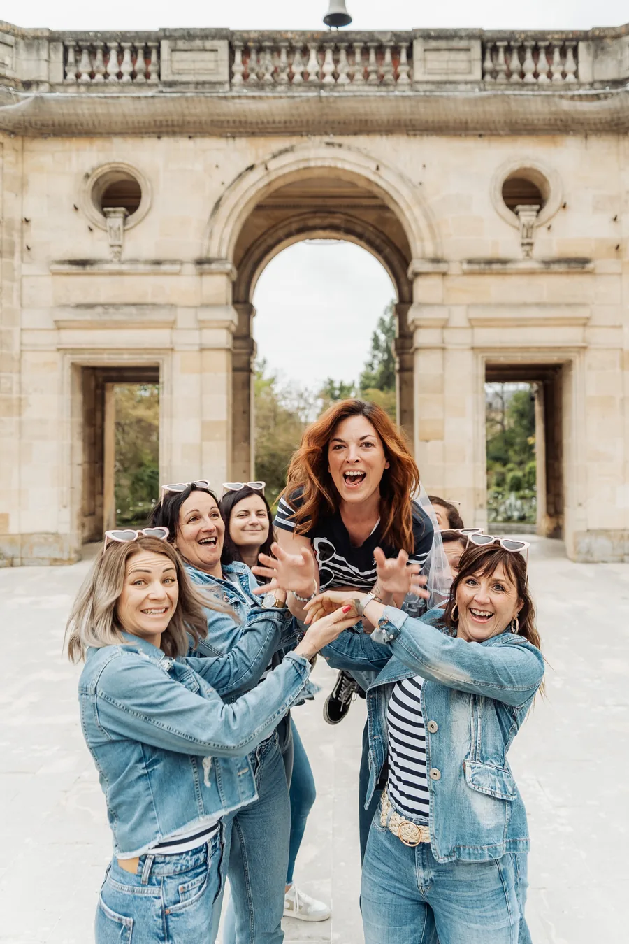 Le groupe qui porte la future mariée à bout de bras sous une arche de pierre, EVJF à Bordeaux