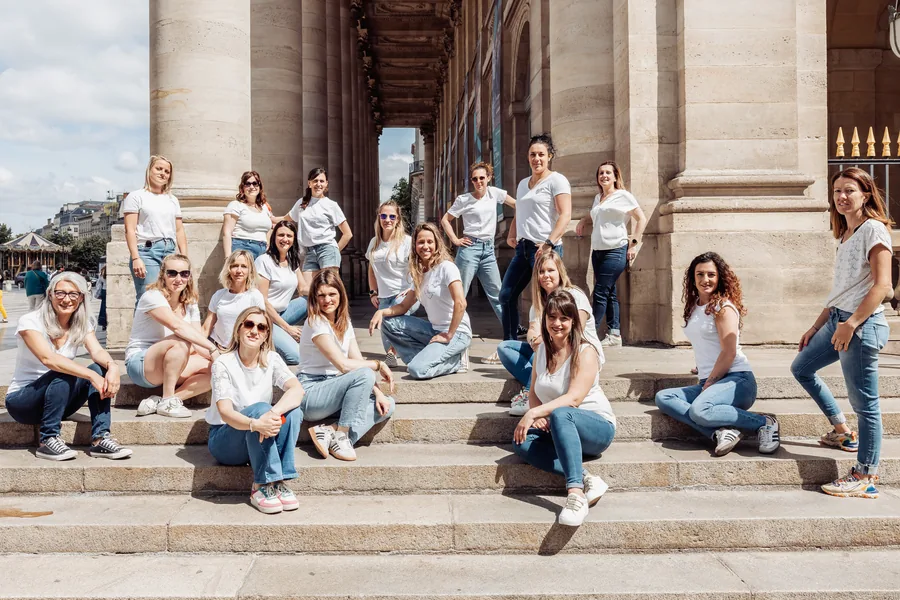 Une quinzaine de participantes en t-shirts blancs et jean, assises sur les marches entre les colonnes, EVJF à Bordeaux