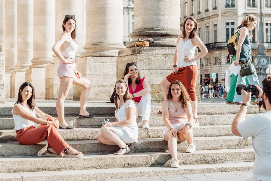 Six copines posées sur les marches d'une colonnade en fin de journée, un photographe au premier plan, EVJF à Bordeaux