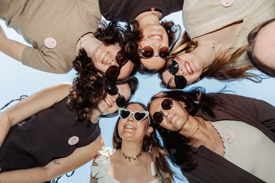 Huit visages penchés en cercle au-dessus de l'objectif, lunettes de soleil et ciel bleu, EVJF à Bordeaux