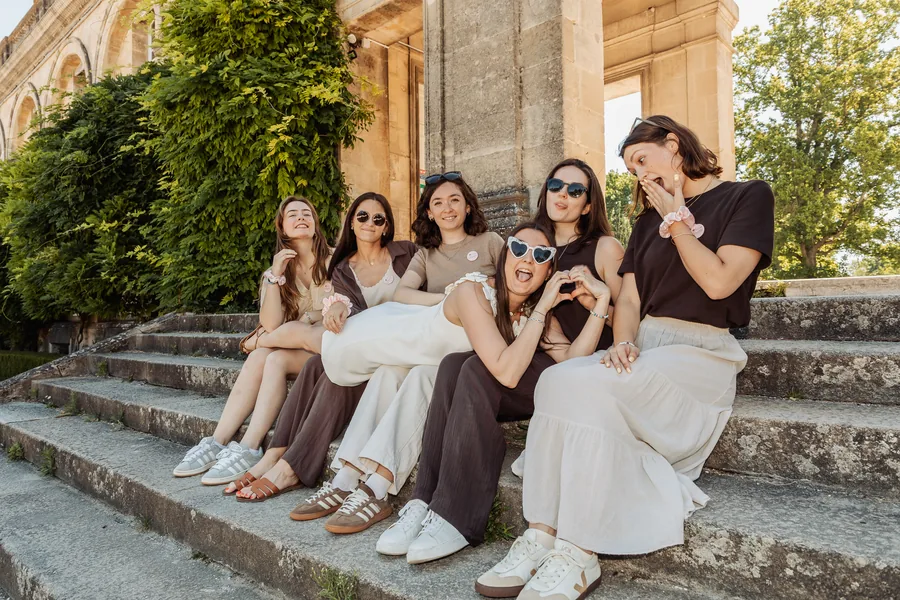 Le groupe assis sur les marches d'un perron, la mariée en robe blanche au centre, EVJF à Bordeaux