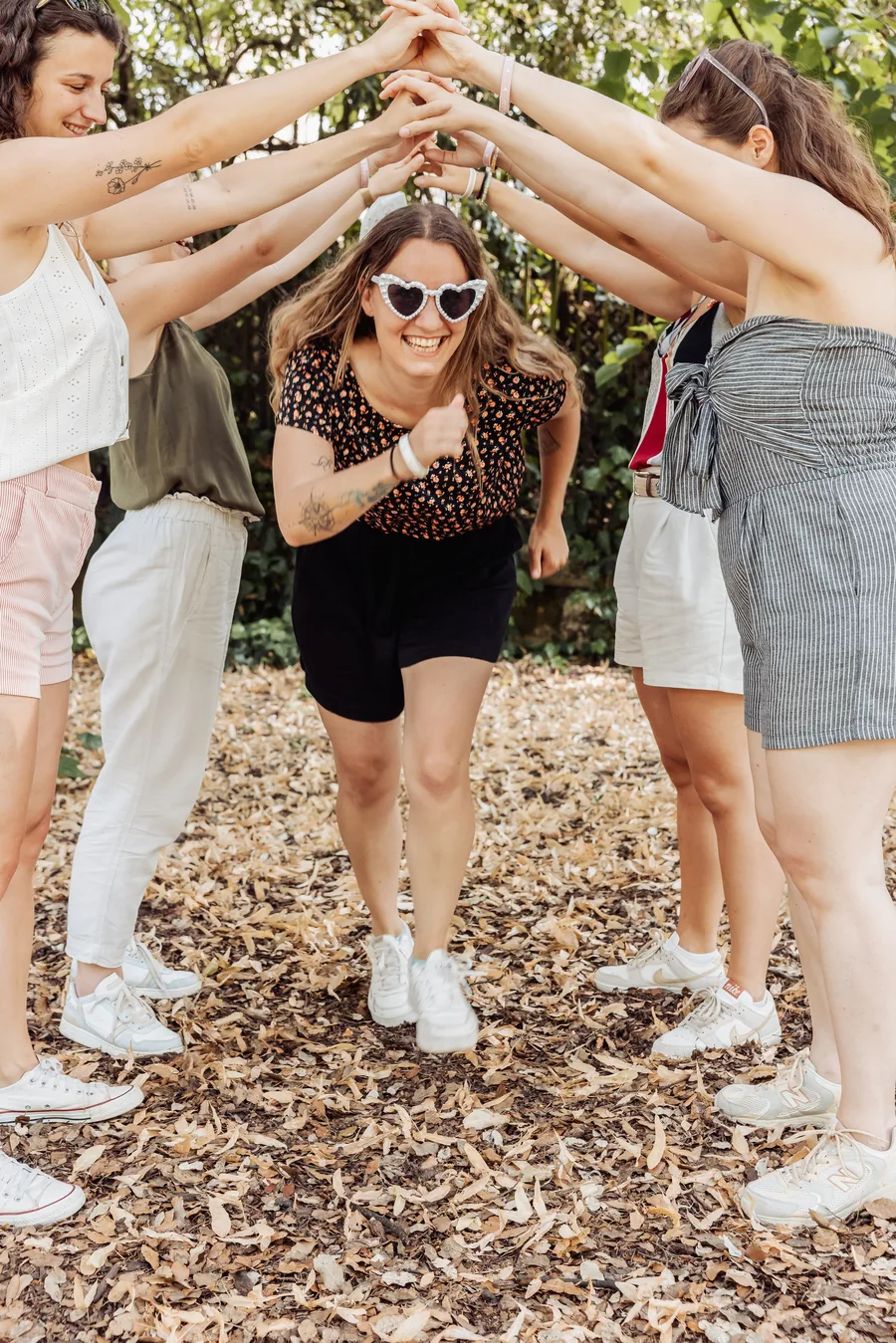 Une amie en lunettes en forme de cœur passe sous une haie de bras levés, sur un sol couvert de feuilles sèches, EVJF à Bordeaux
