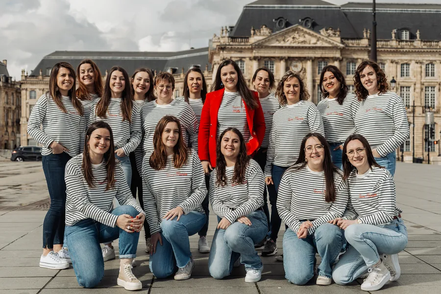 Une quinzaine d'amies en marinières et jean, debout et à genoux sur une place pavée, une veste rouge au centre, EVJF à Bordeaux