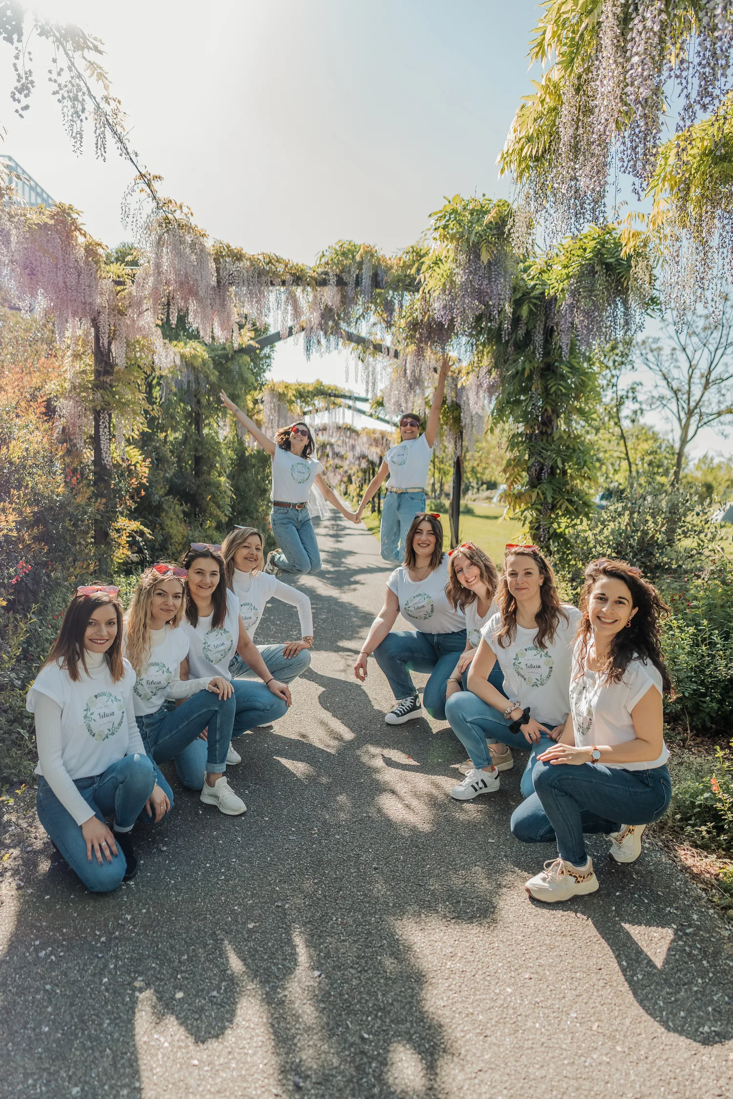 Le groupe sous une allée de glycines en fleurs, certaines accroupies, une amie les bras levés au milieu de l'allée, EVJF à Bordeaux