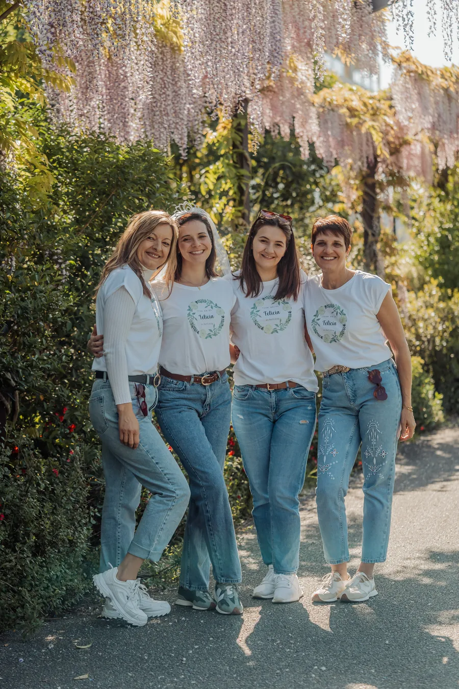 Quatre amies enlacées en t-shirts blancs assortis et jean, la mariée coiffée d'un voile, devant une glycine en fleurs, EVJF à Bordeaux