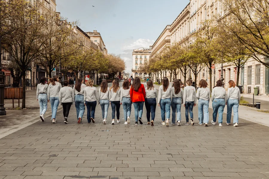Le groupe s'éloigne de dos dans une allée bordée d'arbres, une veste rouge au milieu de la ligne, EVJF à Bordeaux