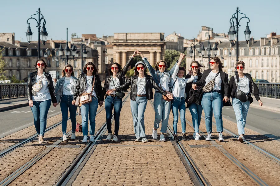 La bande remonte les rails du tram bras levés, les façades bordelaises derrière elle, EVJF à Bordeaux