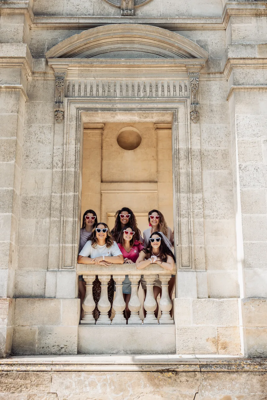Cinq copines accoudées à une balustrade de pierre, sous une grande arche en pierre blonde, EVJF à Bordeaux