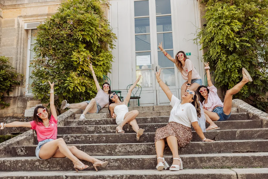 Le groupe assis sur un escalier de pierre, bras levés et éclats de rire, devant une façade couverte de lierre, EVJF à Bordeaux