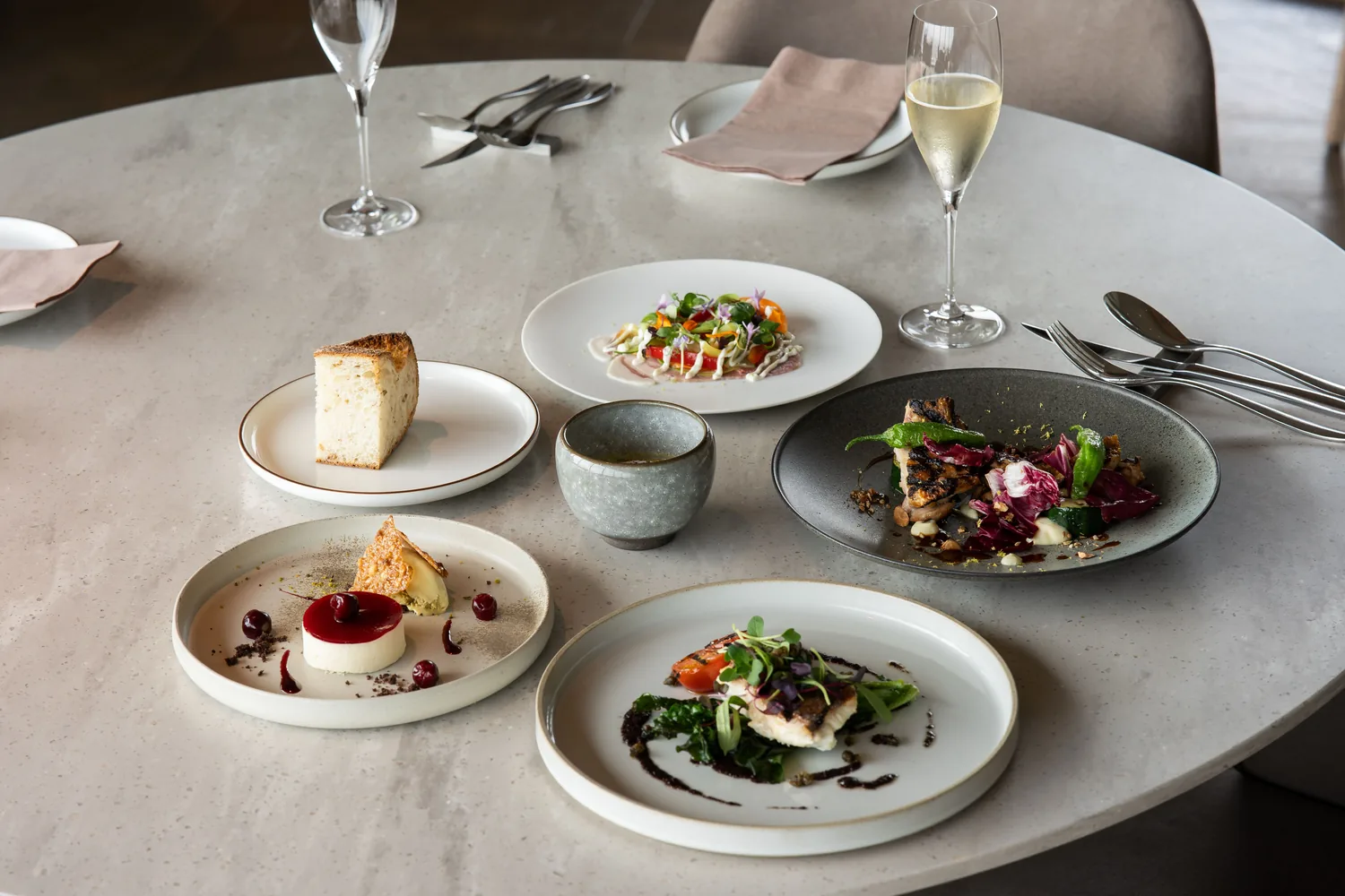 Une table ronde dressée pour le dîner : entrée fleurie, poisson grillé, dessert aux cerises et flûtes de champagne