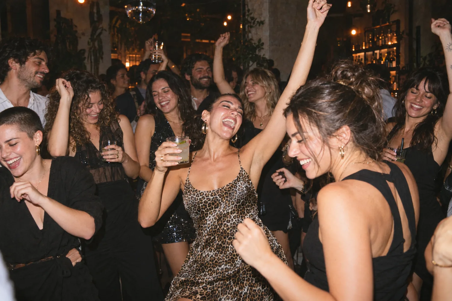 Sur la piste, une amie en robe léopard danse un verre à la main, entourée de copines qui rient