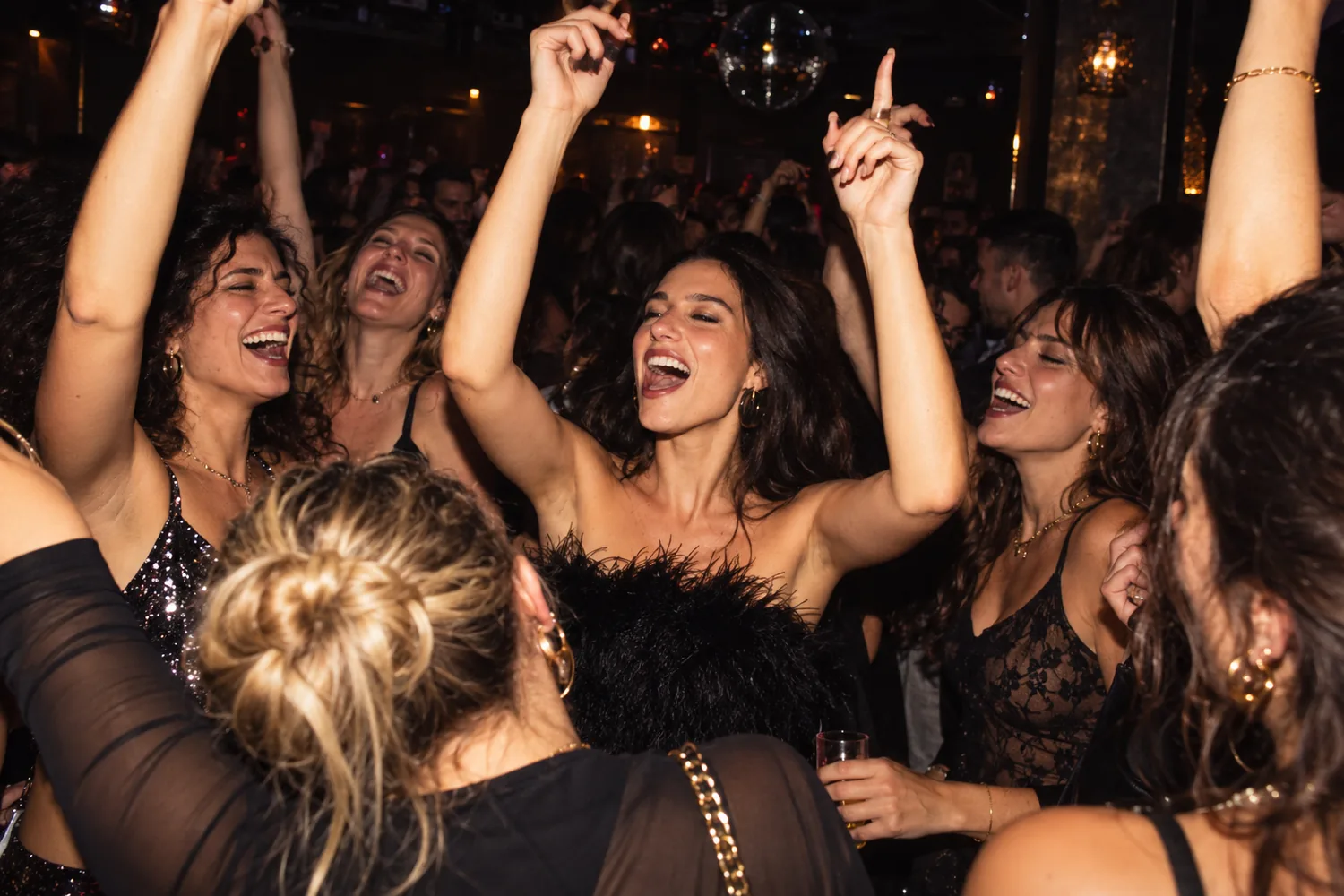 Des amies dansent bras levés et chantent sous une boule à facettes