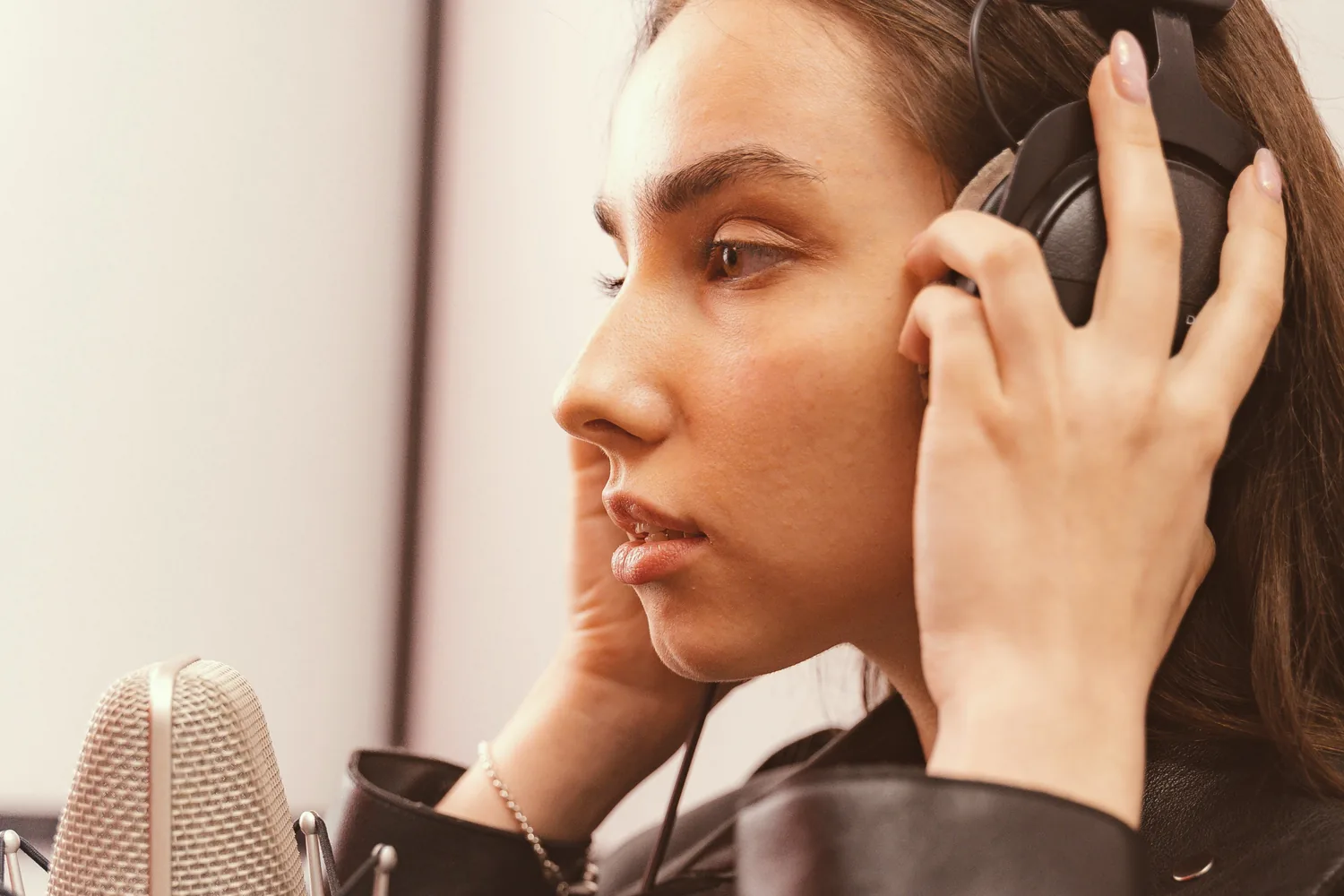 Une chanteuse de profil, casque tenu à deux mains, devant un micro de studio