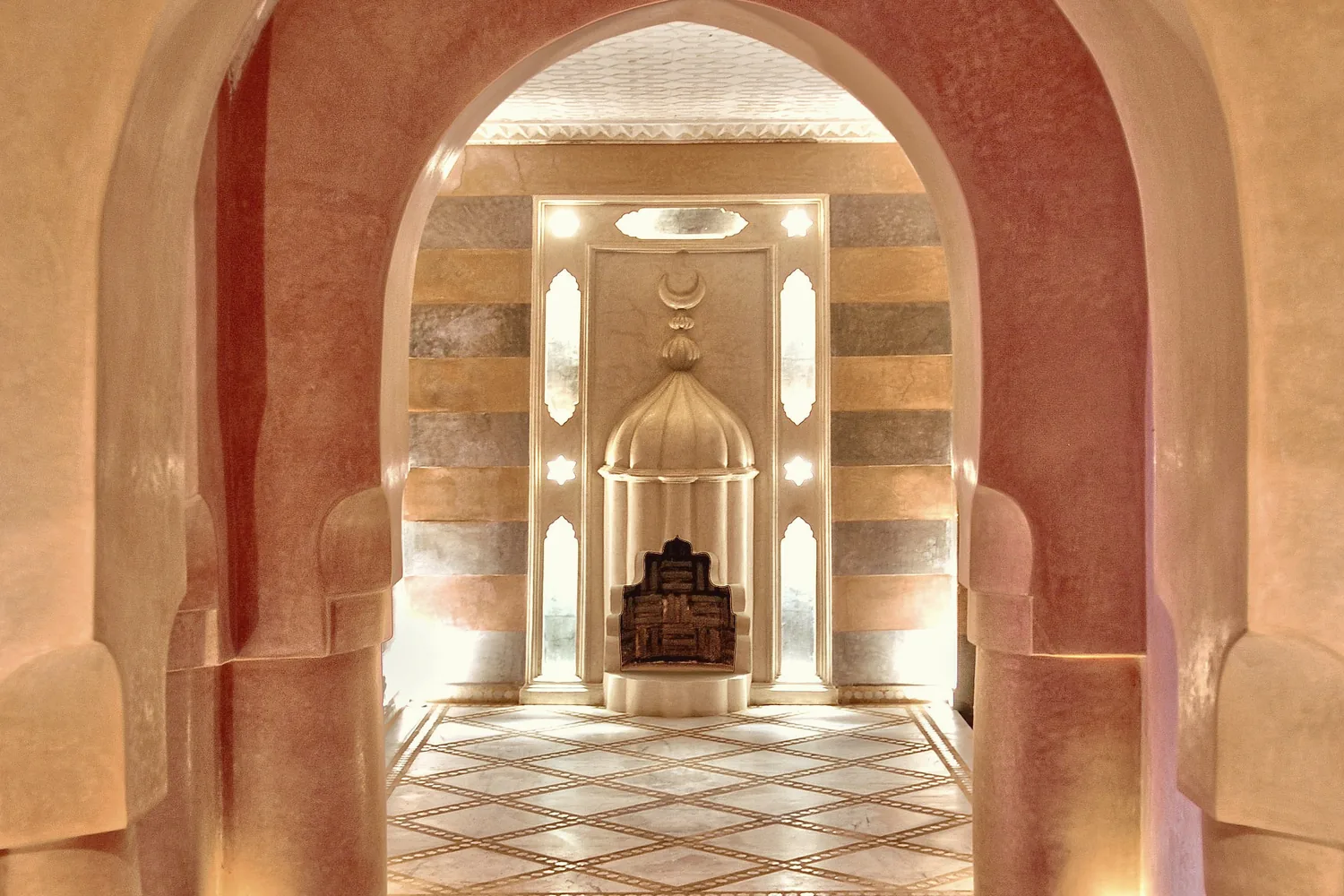 Enfilade d'arches aux murs rose et ocre, ouvrant sur une niche sculptée et un sol de marbre à motifs