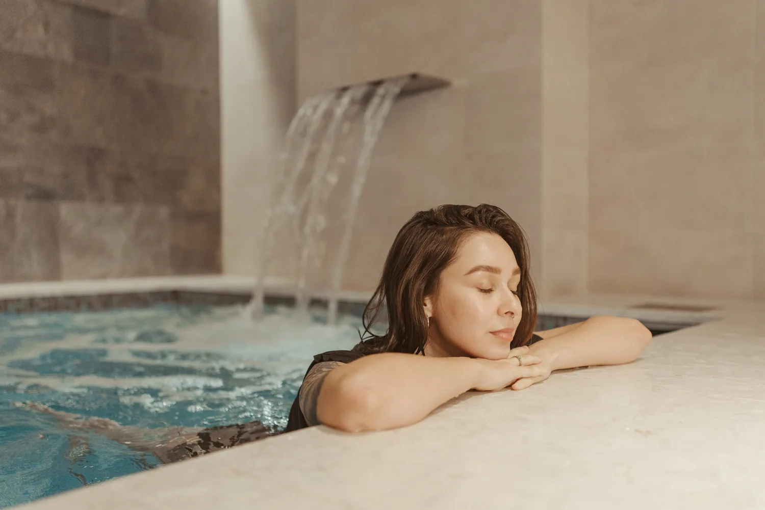 Une femme, les yeux fermés, pose le menton sur ses mains au bord du bassin d'un spa