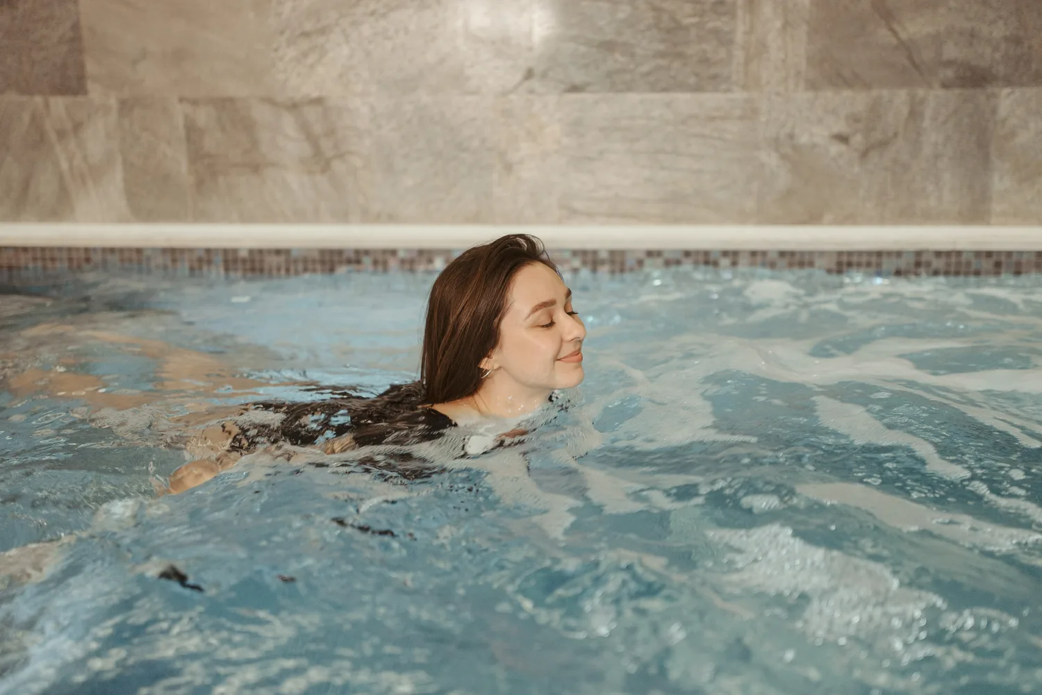 Une femme sourit, les yeux fermés, de l'eau jusqu'aux épaules dans le bassin à remous d'un spa
