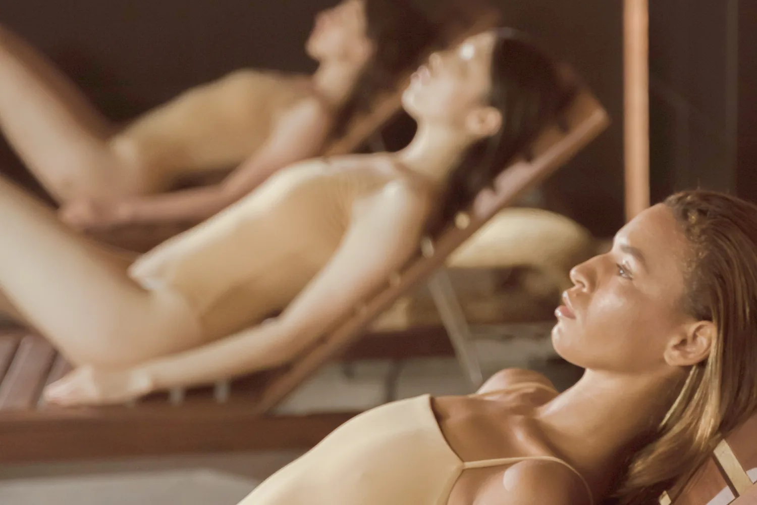 Détente au spa : trois femmes en maillot allongées sur des transats en bois